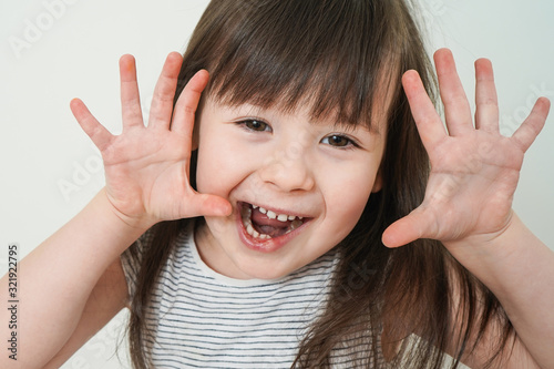 The child indulges in front of the camera. Close-up portrait of a cheerful girl. Girl says boo.