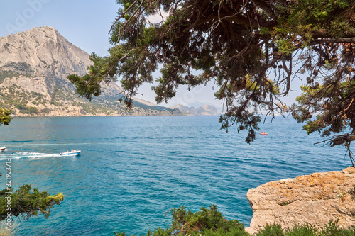 Obraz na płótnie Boat moving on the waves. View of Green Bay, coastal cliffs and a ridge of mountains on the horizon. Mountain juniper. Black Sea coast, Sudak region, Republic of Crimea w salonie