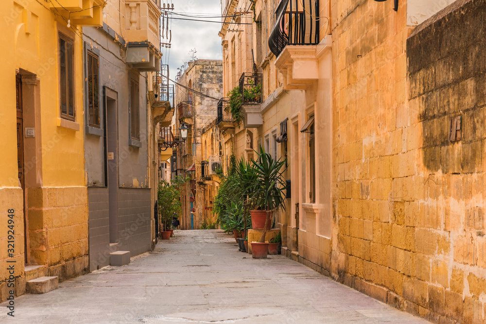 Old medieval street with yellow buildings and flower pots in Birgu, Valletta, Malta