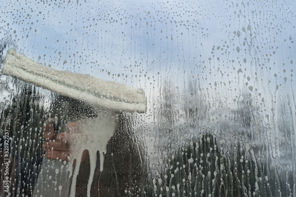 Caucasian man washing glass with microfiber window washer. Spring cleaning concept. Blue sky. Copy space on the right.