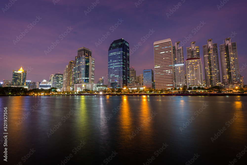 Scenic view of modern skyscrapers behind a lake at the Benjakiti (Benjakitti) Park in downtown Bangkok, Thailand, at dusk.