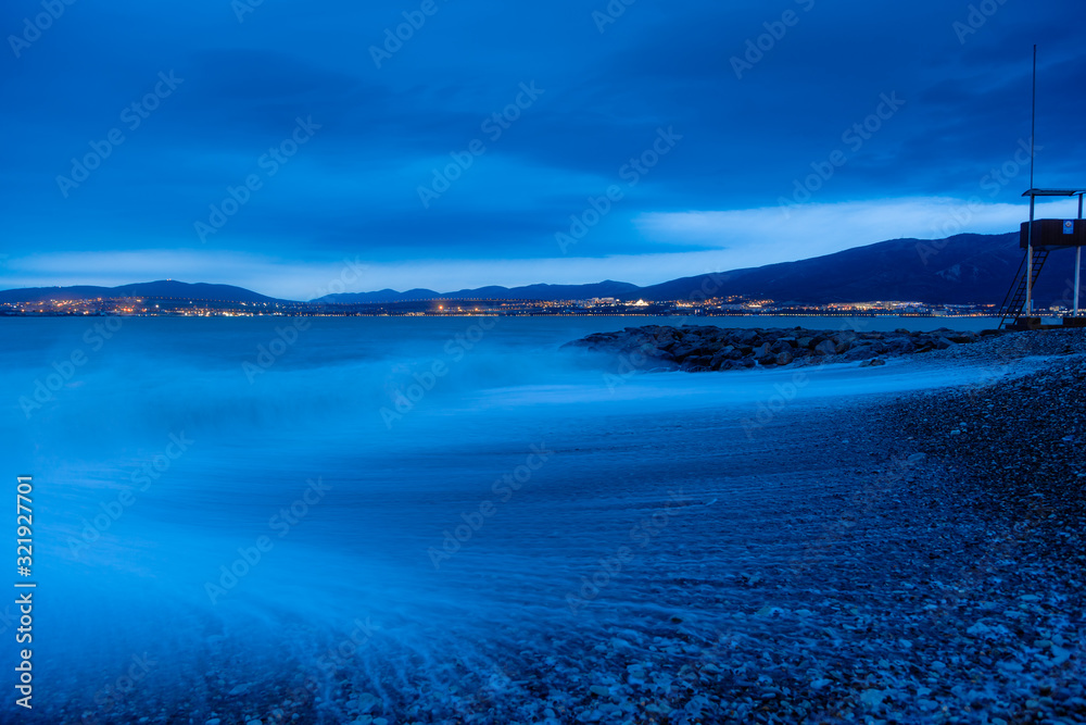 Gelendzhik beach in the evening in a storm. The waves at high speed turn into a blue fog. Pebble beach, breakwater. In the background, the Caucasus mountains, city of Gelendzhik