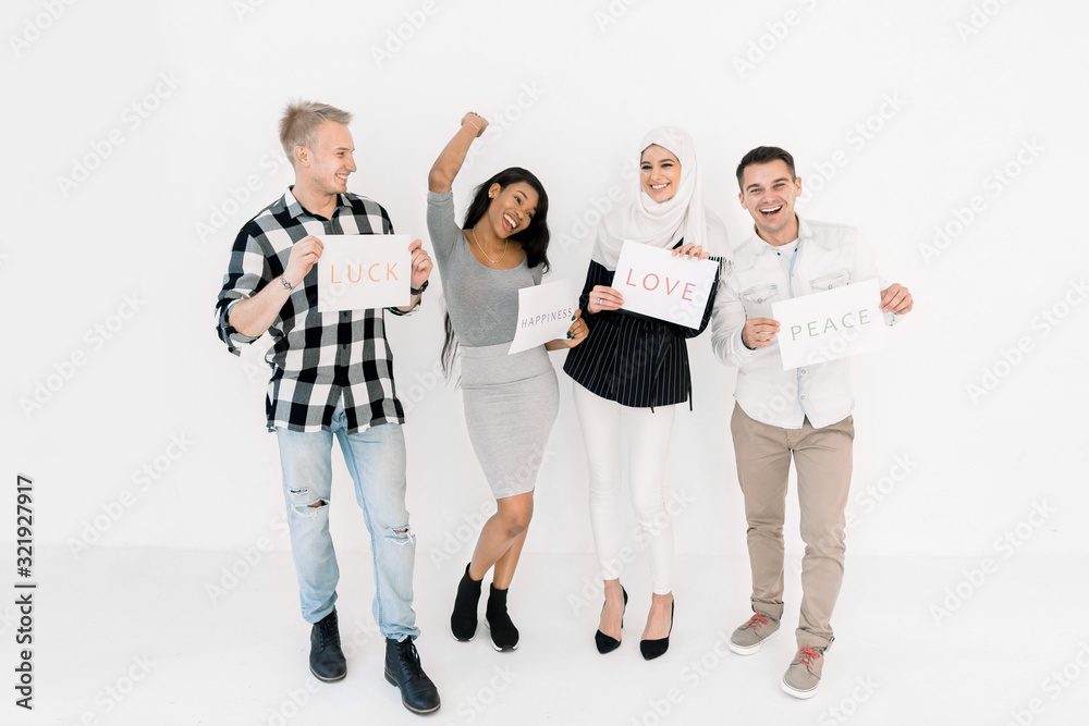 Four young friends, students of different nationalities and religions together over white background, holding banners with positive slogans of love, peace, happiness, luck. Four young friends, students of different nationalities and religions together over white background, holding banners with positive slogans of love, peace, happiness, luck.