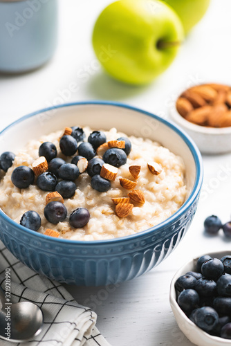 Oatmeal Porridge Bowl With Nuts And Blueberries On White Table. Healthy Breakfast Concept, Vertical Orientation