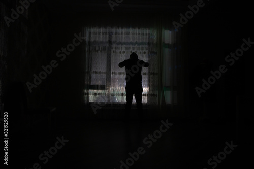 Silhouette of a man standing at a window inside the room. Fantasy picture with old vintage lantern at the window inside dark room.