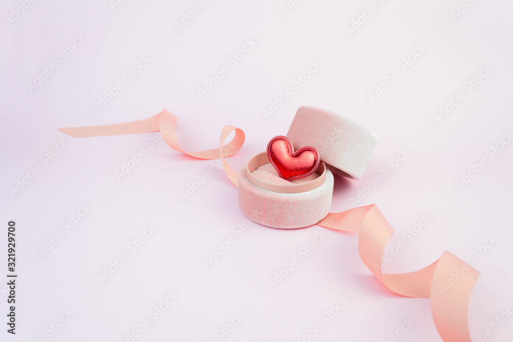 Red heart in a round ring box with ribbon on soft pink background. Gift for a lover, partner, symbol of eternal love for life. Romantic unisex feelings, proposal. Banner template with copy space Red heart in a round ring box with ribbon on soft pink background. Gift for a lover, partner, symbol of eternal love for life. Romantic unisex feelings, proposal. Banner template with copy space