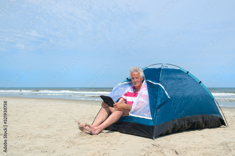 Man with digital tablet camping in shelter at the beach