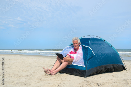 Man with digital tablet camping in shelter at the beach © Ivonne Wierink