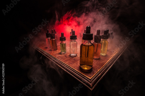 Smoke clouds and vape liquid bottles on dark background. Light effects. Useful as background or vape advertisement or vape background. Selective focus