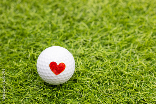 Golf ball with red heart on golf ball on green grass background