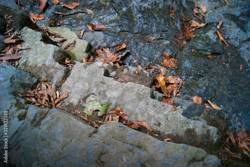 Stone descent to the mountain river, natural steps are sprinkled with orange fallen leaves. Autumn in the mountains.
