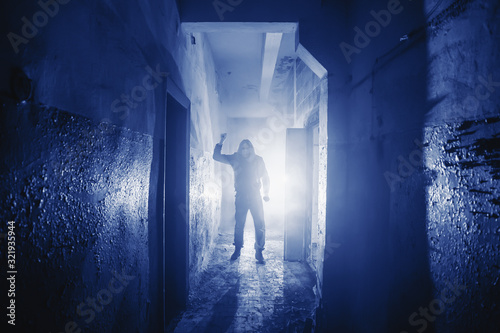 Dangerous Murderer or killer with Knife in hand and light from back in scary corridor in Phantom Blue color toned.