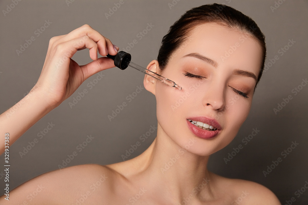 Close-up elegant young lady applies face oil.