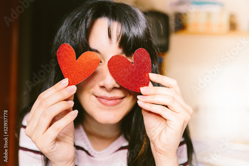 Happy brunette woman with red glitter heart shaped cardboard in her eyes smiling on valentines day. Valentine's day and fall in love concept.