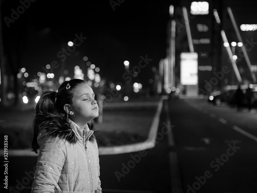 Little girl with closed eyes staying in dark in front of shopping mall lights