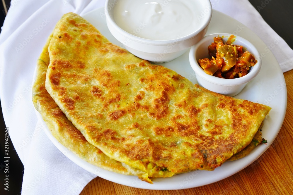 A plate with aloo paratha bread stuffed with potatoes and a dish of yogurt at an Indian restaurant A plate with aloo paratha bread stuffed with potatoes and a dish of yogurt at an Indian restaurant