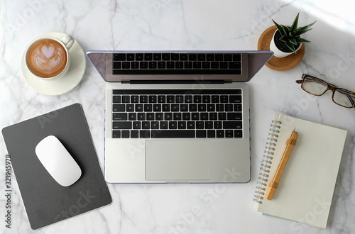Flat lay workspace. Woman hand with coffee cup, smartphone, computer, notebook, planner and stationary with copy space on marble table background. Top view.