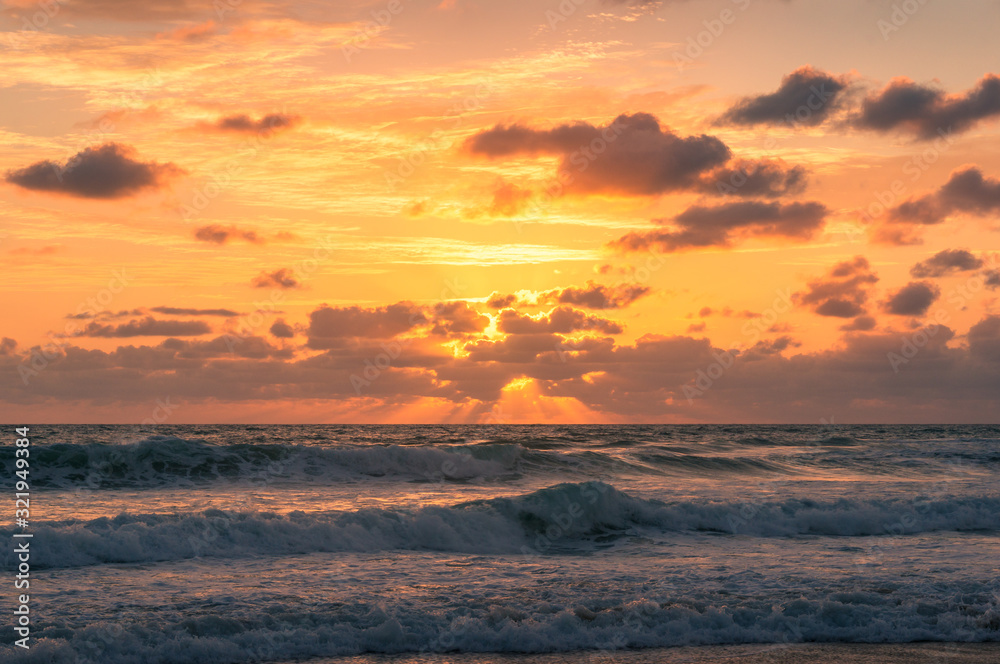 Beautiful sunrise seascape with colorful golden orange clouds and soft waves