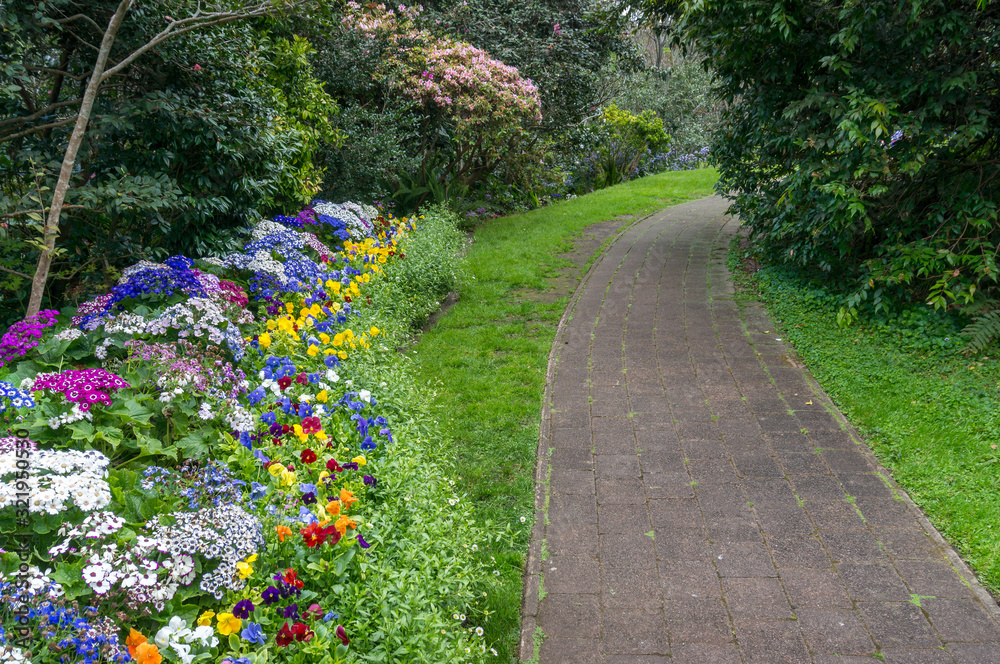 Spring park alley with colorful blooming flowerbeds and green grass