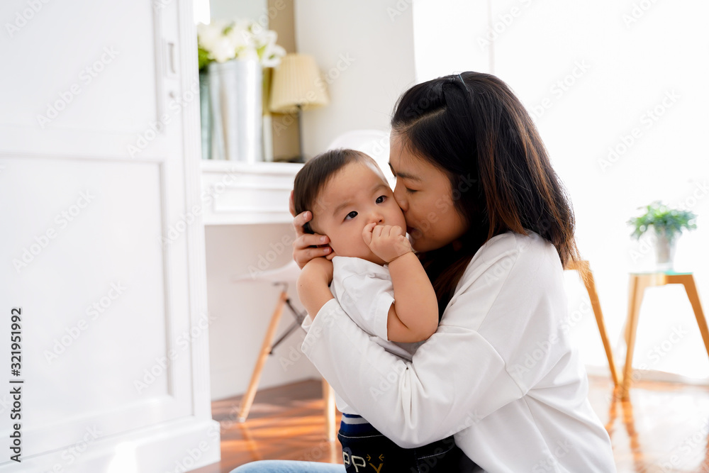 Asian young adult mother kissing joyful son in living room. Love of mother concept. Asian young adult mother kissing joyful son in living room. Love of mother concept.