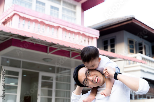 Asian father giving a piggyback ride for little son in front of the house. Dad and child enjoying warm family time