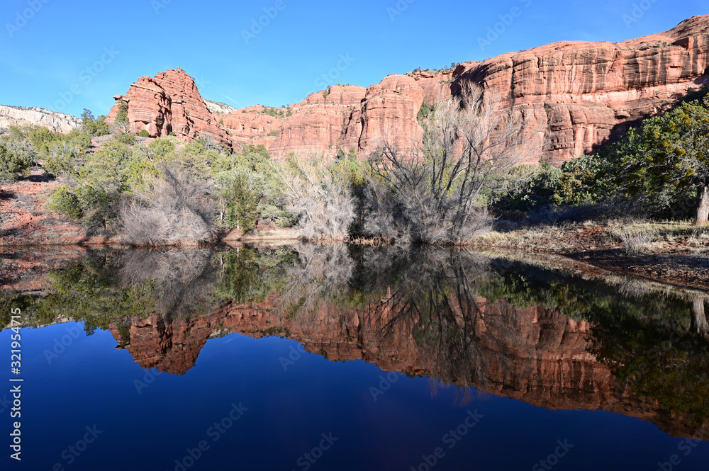 Red rock formations reflected in tranquil pond in Sedona, Arizona backcountry on clear cloudless winter afternoon.