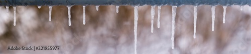 panoramic view of icicles on snow bokeh background. icicles on a metal crossbar © mijun