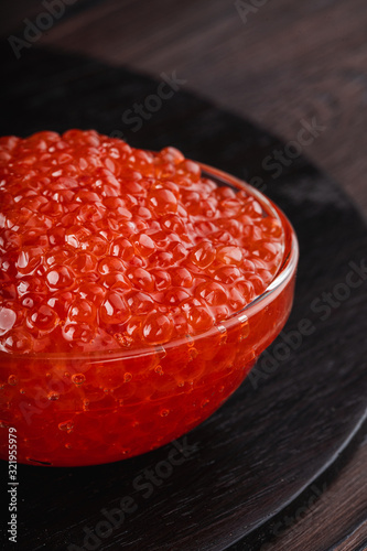 Close up of red caviar in a bowl on a dark wooden table