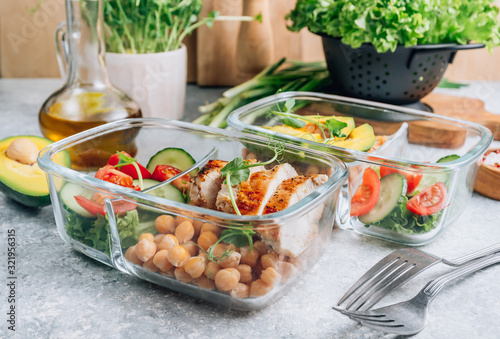 Healthy meal prep containers with chickpeas, chicken, tomatoes, cucumbers and avocados. Healthy lunch in glass containers on light gray background. Zero waste concept. Selective focus. photo