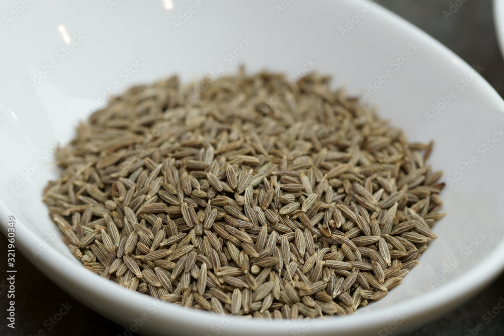 Cumin seeds in a bowl on grey background with copy space.
