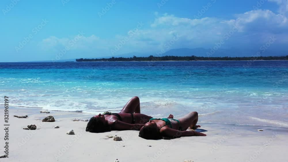 Two female friends relaxing on the shore of a beautiful beach, soaking up the warm sun Two female friends relaxing on the shore of a beautiful beach, soaking up the warm sun