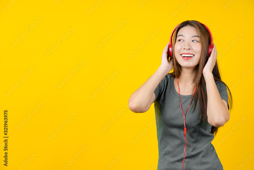 Happiness Asian smiling young woman wearing technology wireless headphones for listening the music via smart mobile phone on isolated yellow color background, Lifestyle and leisure with hobby concept Happiness Asian smiling young woman wearing technology wireless headphones for listening the music via smart mobile phone on isolated yellow color background, Lifestyle and leisure with hobby concept