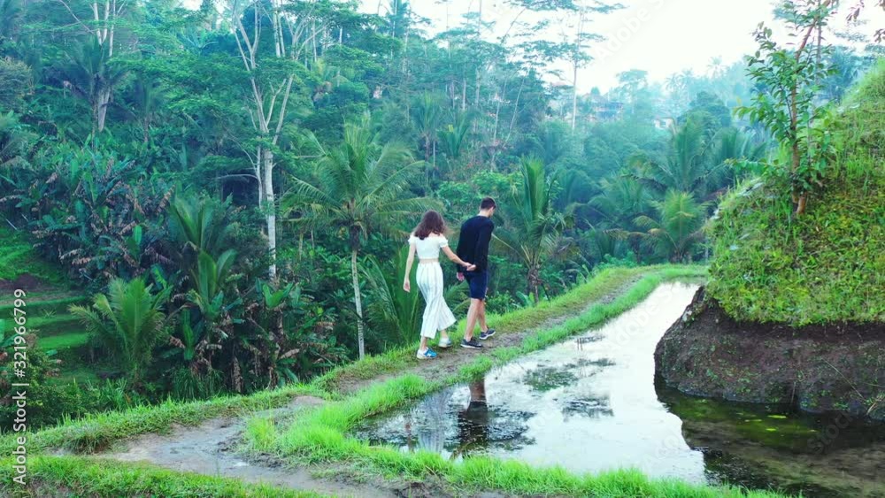 Young man and woman walking around a wet cliff whilst exploring a rice field farm in Indonesia Young man and woman walking around a wet cliff whilst exploring a rice field farm in Indonesia