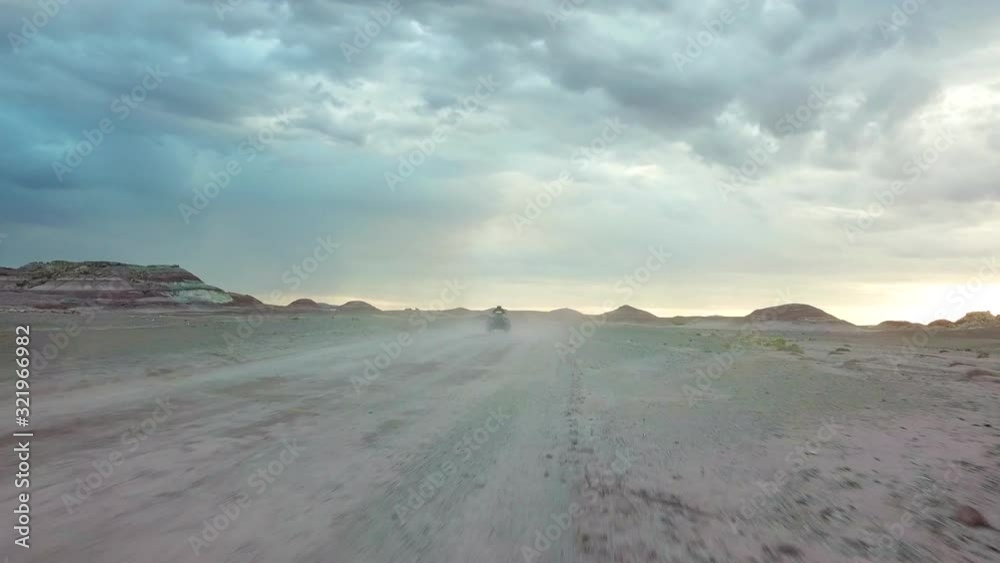Dynamic Tracking Aerial View of ATV Vehicle Moving Fast on Dusty Road in Dry Deset Landscape Under Dramatic Sky Dynamic Tracking Aerial View of ATV Vehicle Moving Fast on Dusty Road in Dry Deset Landscape Under Dramatic Sky