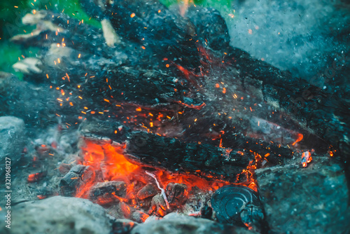 Vivid smoldered firewoods burned in fire closeup. Atmospheric background with orange flame of campfire. Full frame image of bonfire with sparks in bokeh. Warm vortex of glowing embers and ashes in air