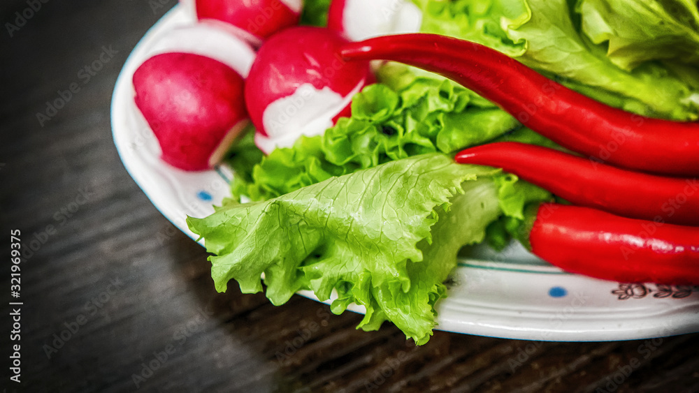 fresh vegetables - radish , pepper, salad in a plate on a wooden surface, blurred background