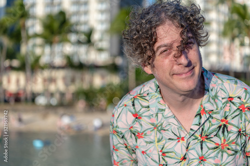 Portrait of a stylish middle aged man visiting Hawaii and enjoying vacation time at the beach. Wind blows his long curly hair over his eyes.