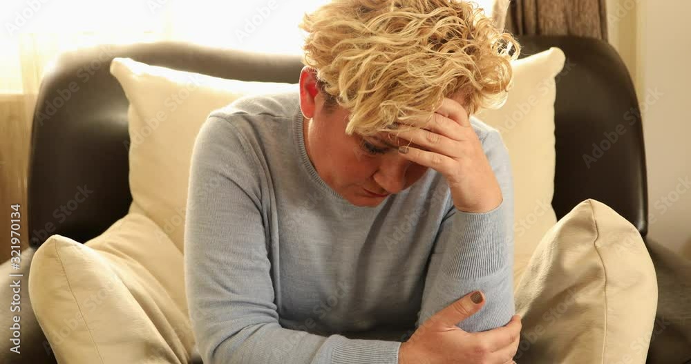 Middle aged sad woman with in depression sitting on sofa at home Middle aged sad woman with in depression sitting on sofa at home
