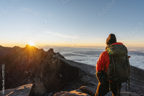 a man with backpack enjoying sunrise over the clouds on Kota Kinabalu summit in Malaysia. Travel lifestyle, adventure and outdoor activity concept