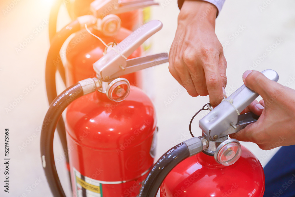 Hand pulling safety pin from red fire extinguisher. Hand pulling safety pin from red fire extinguisher.