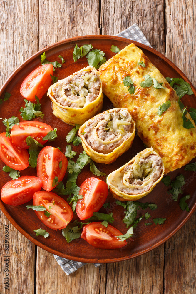 omelet roll stuffed with meat, cheese and pickles close-up in a plate. Vertical top view omelet roll stuffed with meat, cheese and pickles close-up in a plate. Vertical top view