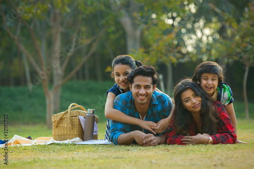 Happy man and woman on a picnic lying down in garden beside a picnic basket and their children lying on their backs.