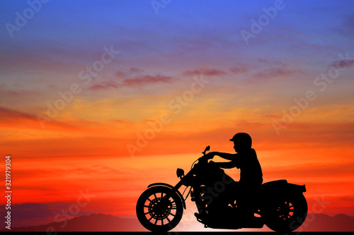 Silhouette biker with his motorbike beside the natural lake and beautiful sunset sky. © rathchapon
