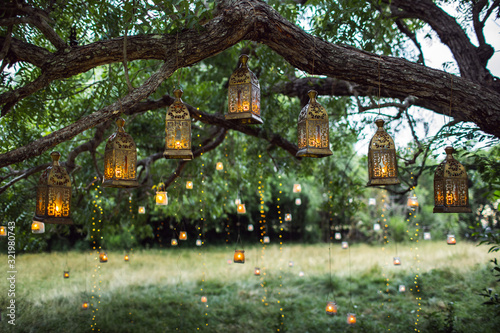 Evening wedding ceremony with a lot of vintage lanterns, lamps, candles. Unusual outdoor ceremony decoration. Beautiful garden party concept.