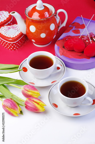 Tea for two. Two cups of tea, a bouquet of tulips, a porcelain teapot, gifts on a table with a white tablecloth.