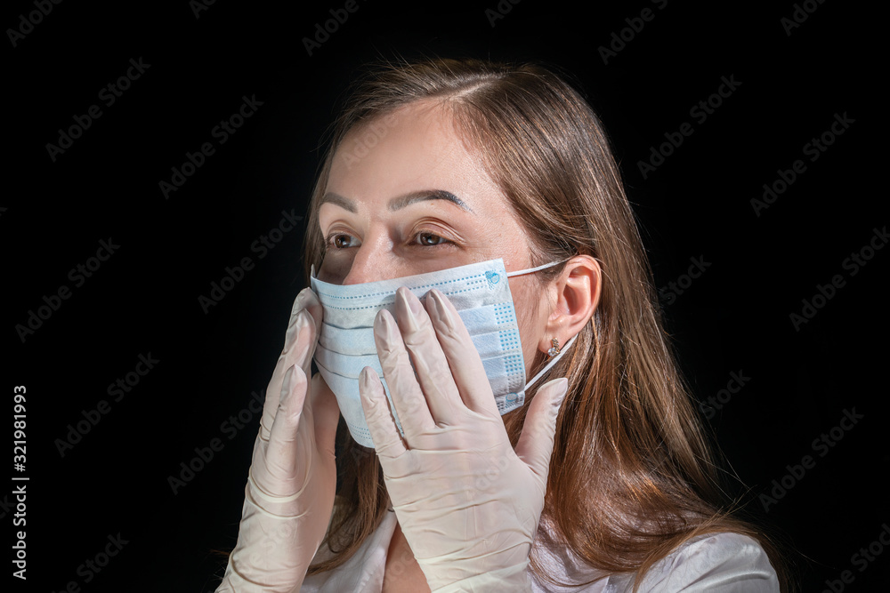 Young female doctor puts on white protection mask on dark background Young female doctor puts on white protection mask on dark background