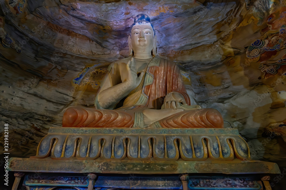 Painted statue of buddha sitting on top of an altar inside a cave. Yungang Grottoes  near Datong, Shanxi Province, China