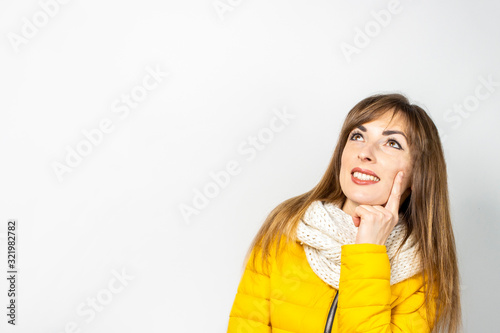 Woman in a jacket and scarf looks up on a white background. Concept dream, planning, pensive, surprise