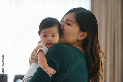 Mother kiss baby cheek when holding him. Mother places baby on the shoulder with happy family.