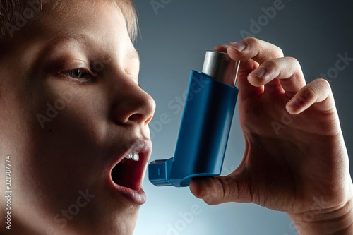 Portrait of a boy using an asthma inhaler to treat inflammatory diseases, shortness of breath. The concept of treatment for cough, allergies, respiratory tract disease. photo